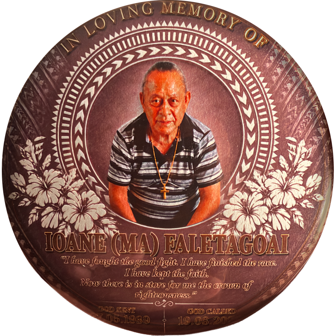 A round memorial pin for Marcus's grandad, Ioane (Ma) Faletagoai: his photo inside patterned bands and hibiscus flowers, with In loving memory of around the top